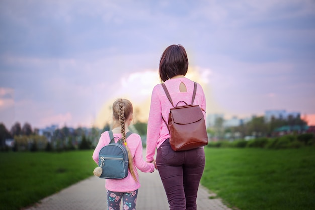 Madre y su pequeña hija con mochila caminando en día de verano. Vista desde atrás.