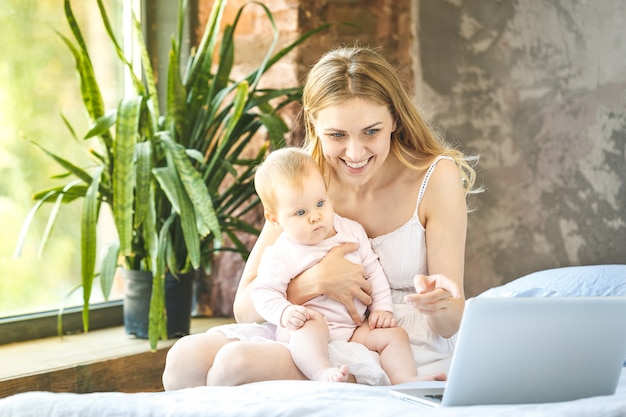 Madre y su pequeño bebé en casa. Madre con su bebé viendo algo en la computadora portátil.