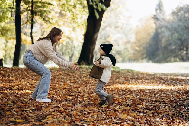 Madre con su pequeño hijo caminando en el parque otoñal