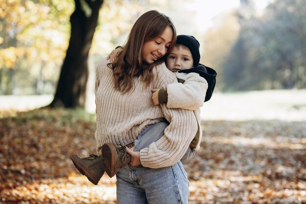 Madre con su pequeño hijo caminando en el parque otoñal