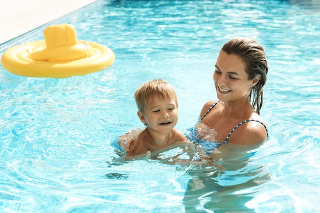 Madre y su pequeño y lindo hijo nadando en la piscina al aire libre durante las vacaciones de verano