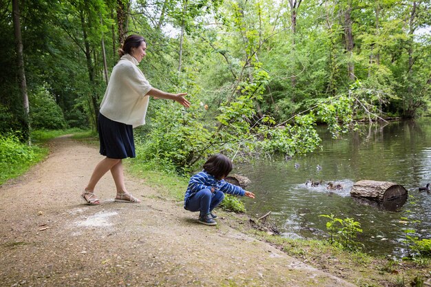 Madre y su pequeño niño lindo alimentando patos en el estanque de un parque. Ocio familiar