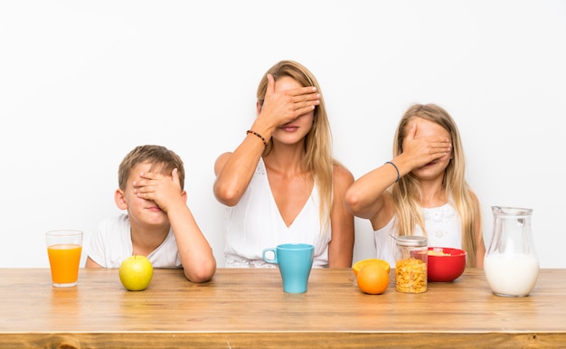 Madre con sus dos hijos desayunando y cubriéndose los ojos