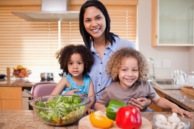 Madre y sus hijas preparando ensalada en la cocina juntos