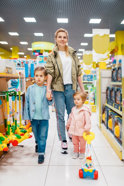 Madre con sus hijos pequeños en la tienda de niños. Mamá con hija e hijo juntos eligiendo juguetes en el supermercado, compras familiares