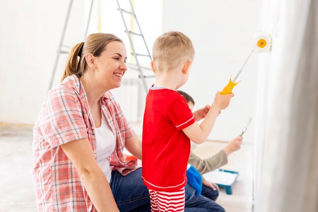 Madre con sus hijos pintando la pared con pintura usando rodillo y pincel