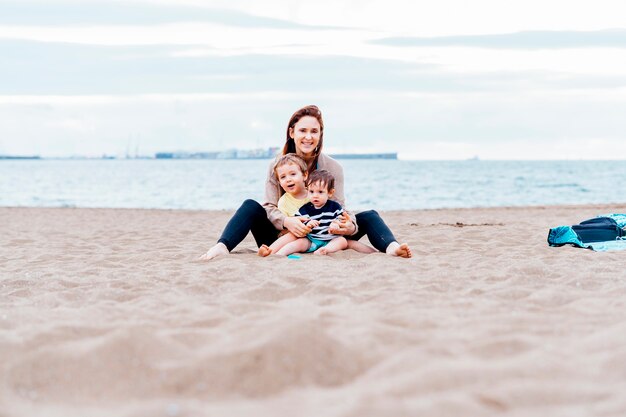 Madre con sus hijos de uno y tres años en la playa en un día nublado de verano. madre soltera