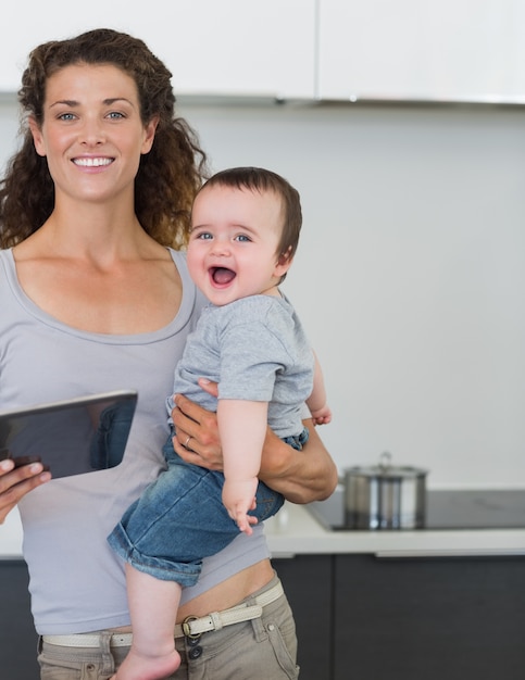 Madre con tableta que lleva al bebé alegre