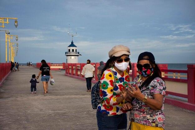 La madre tailandesa mayor y las mujeres jóvenes que usan máscaras de tela visitan el viaje y posan un retrato para tomar una foto en el puente rojo Saphan saranwithi en la playa de la bahía de Prachuap en Prachuap Khiri Khan Tailandia