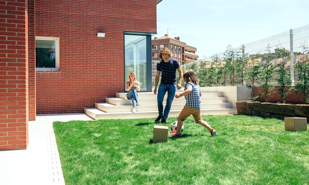 Madre tomando una foto móvil de su esposo e hijo jugando en el jardín