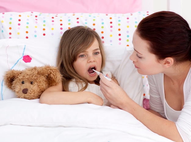 Madre tomando la temperatura de su hija con un termómetro