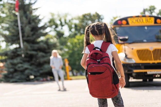 Foto madre trae a su hija a la escuela cerca del autobús escolar. de vuelta a la escuela