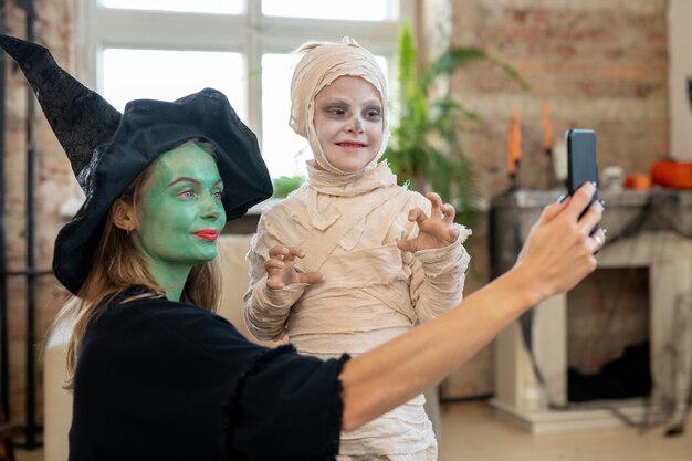 Madre en traje de bruja haciendo selfie con su hijo en traje de zombie