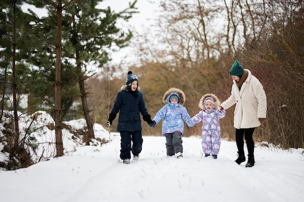 Madre con tres hijos cogidos de la mano y caminando en el bosque de invierno