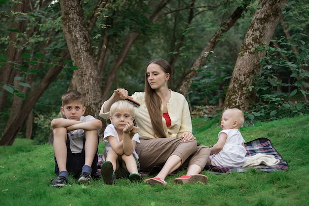 Madre y tres hijos en el parque en el claro. Picnic familiar al aire libre.