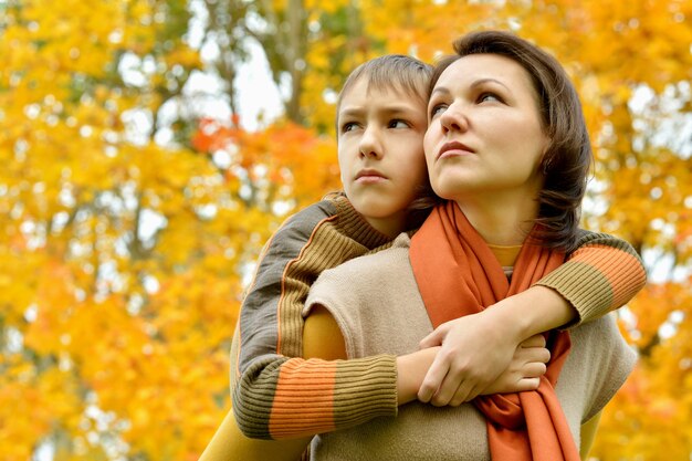 Madre triste con un hijo en un paseo durante la caída de las hojas en el parque