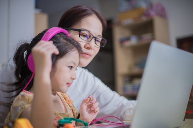 Una madre usa audífonos para que su hija la ayude a estudiar en línea.