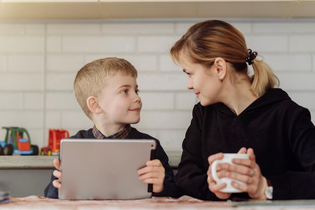Madre usando una computadora portátil y una tableta enseñando con su hijo en línea en su casa en su habitación
