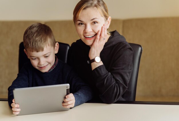 Madre usando una computadora portátil y una tableta enseñando con su hijo en línea en su casa en su habitación