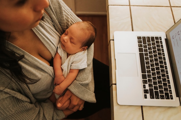 Madre usando una computadora y sosteniendo a su bebé