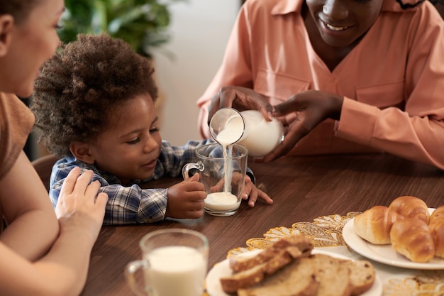 Madre vertiendo leche en vaso para su pequeño hijo en la mesa del desayuno