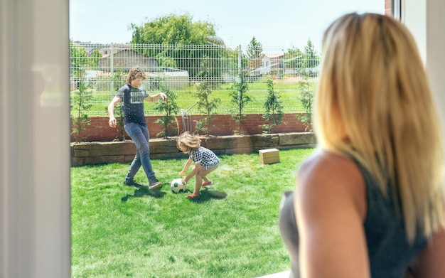 Madre viendo a su esposo e hijo jugando fútbol en el jardín