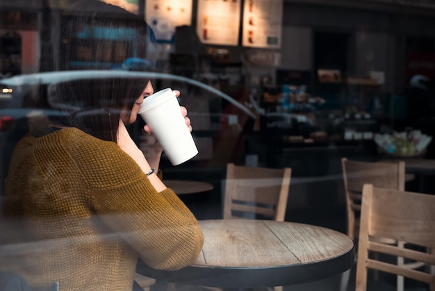 Foto madrid, spanien, 8. april 2021 ein junger mann macht eine pause mit einem cappuccino in einer papiertasse in einer starbucks-kaffeehütte. aufnahme von draußen mit der reflexion des verkehrs und des stadtlebens im fenster