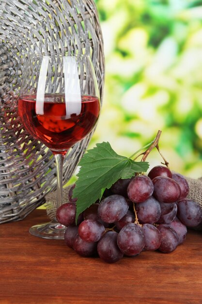 Maduras deliciosas uvas com copo de vinho na mesa no fundo brilhante