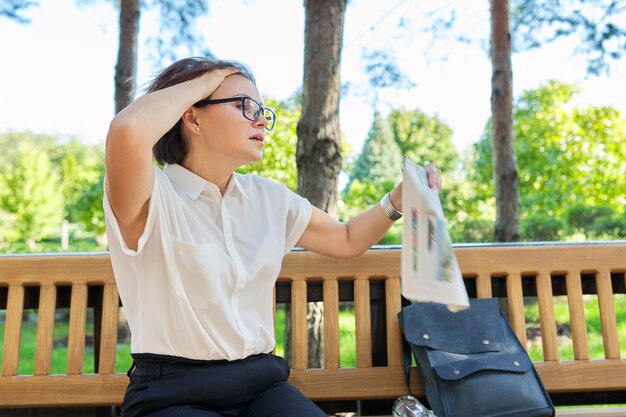 Madurez, mediana edad, salud, menopausia, concepto de edad. Síntomas de la menopausia en la mujer madura, la mujer agita el periódico para refrescarse, siente calor, cambios hormonales de la edad