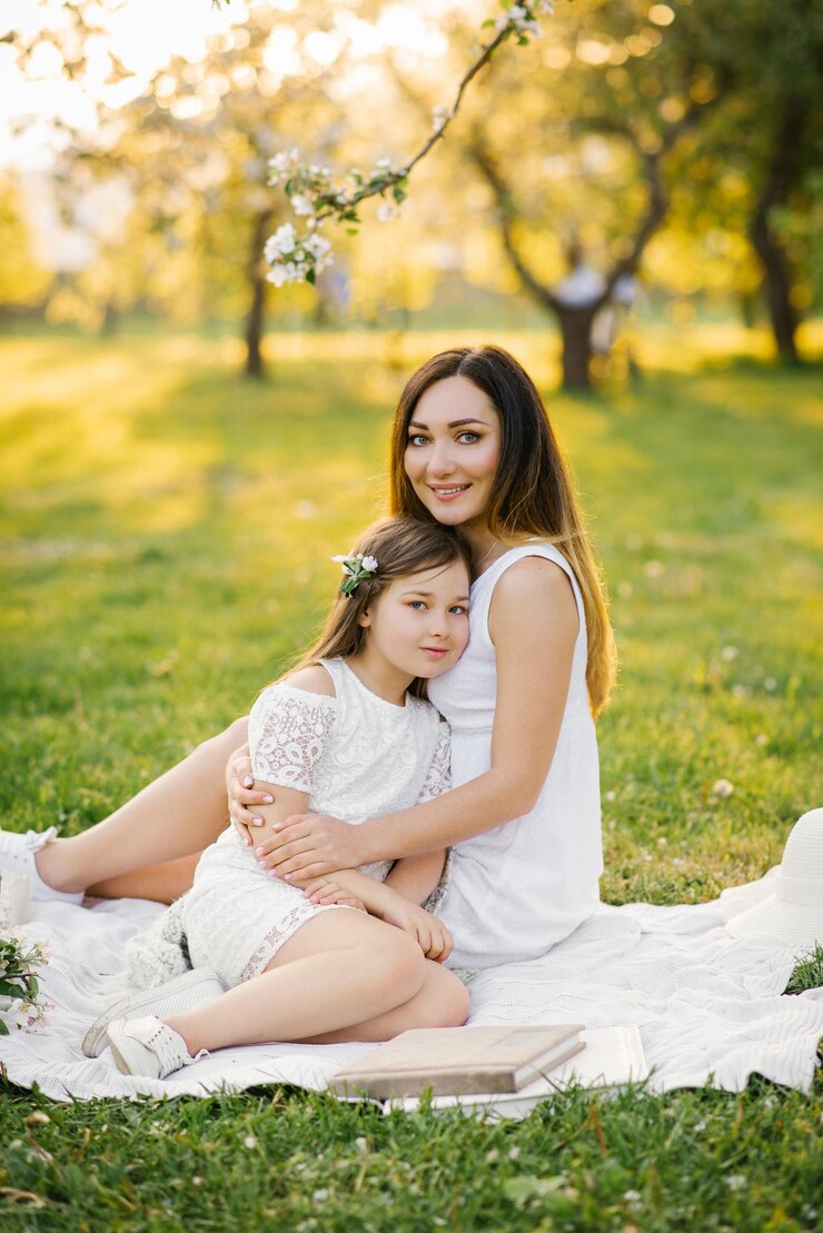 Mãe abraça sua filha sentada em um cobertor em um jardim de primavera Amor materno por uma criança
