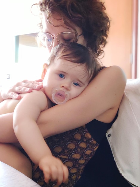 Mãe abraçando filha enquanto está sentada no sofá em casa