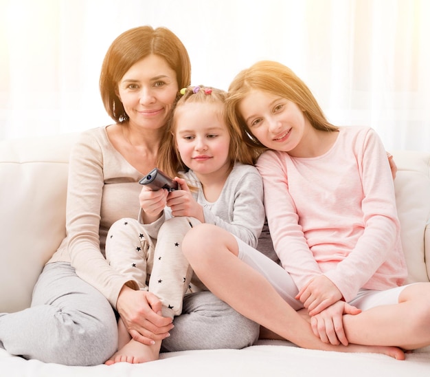 Mãe abraçando filhas enquanto assiste TV em casa