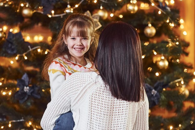 Mãe abraçando sua filha no quarto decorado de natal.