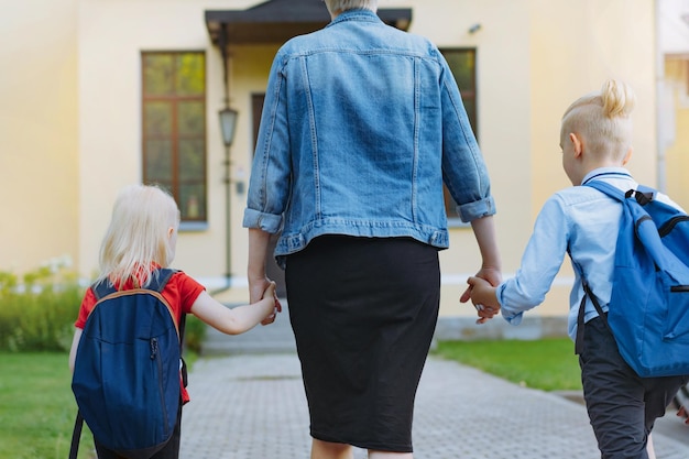 Mãe acompanha crianças à escola de mãos dadas