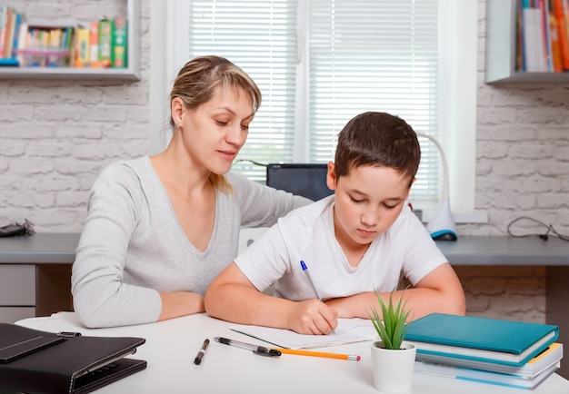 Mãe ajuda filho a dar aulas. O tutor se envolve com a criança, ensina a escrever e contar.