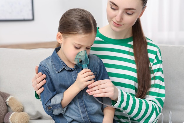 Foto mãe ajudando sua filha doente com inalação de nebulizador em casa