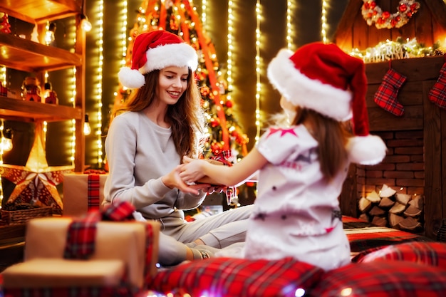 Mãe alegre e sua filha filha troca de presentes. Pai e filhos se divertindo perto de árvore dentro de casa. Família amorosa com presentes na sala de Natal.