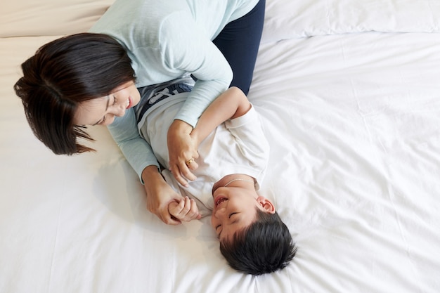 Mãe alegre fazendo cócegas em seu filho feliz e sorridente, vista de cima