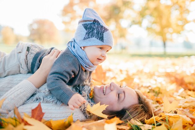 Mãe alegre feliz com seu bebê adorável, deitado no Outono folhas ao ar livre.