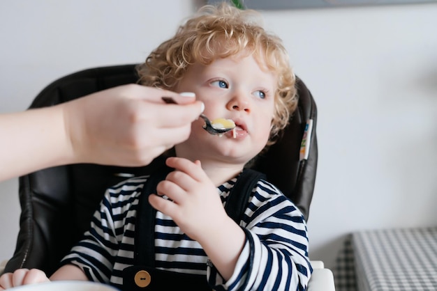 Mãe alimenta seu filho pequeno encaracolado com uma deliciosa sopa um café da manhã em família