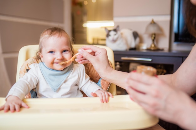 Mãe alimenta sua filha com purê de frutas de uma colher primeira comida