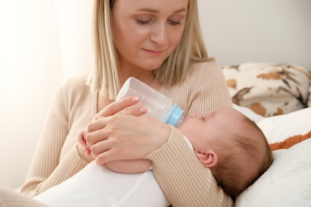 Mãe alimenta um bebê recém-nascido com uma garrafa que o sol está brilhando ao fundo