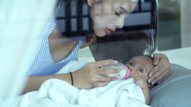 Foto mãe alimentando o leite de seu filho bonito visto através de uma janela de vidro