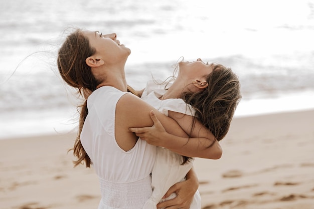 Mãe amorosa abraçando filha fofa na praia de areia