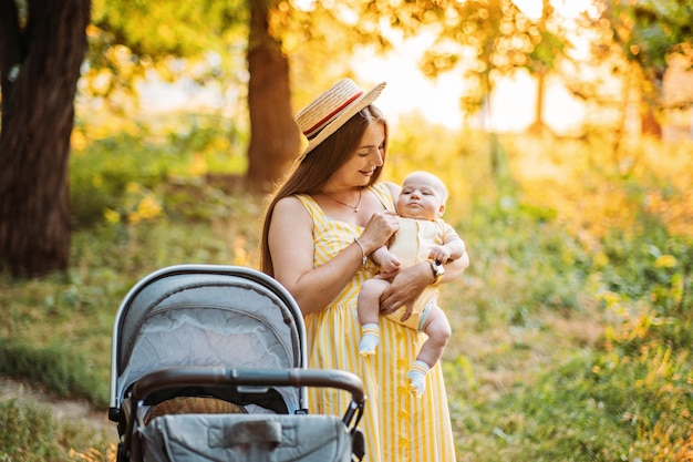 Mãe andando com bebê recém-nascido no carrinho de berço no parque de verão em carrinhos de dia ensolarado para