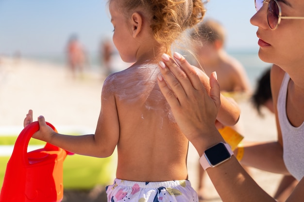 Mãe aplica protetor solar nas costas da filha