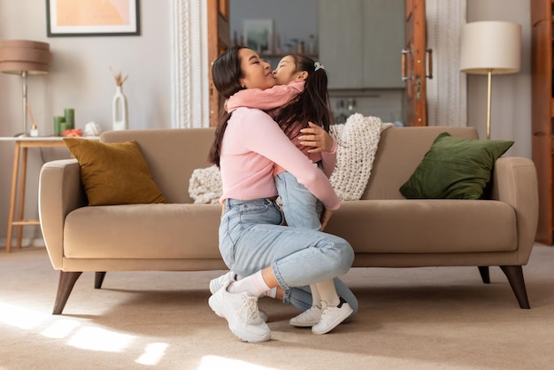 Foto mãe asiática abraçando menina expressando amor e carinho dentro de casa