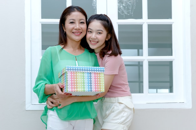 Mãe asiática alegre e filha adolescente segurando a caixa de presente