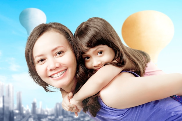Mãe asiática carregando sua filha nas costas com um balão de ar colorido voando com o fundo da cidade