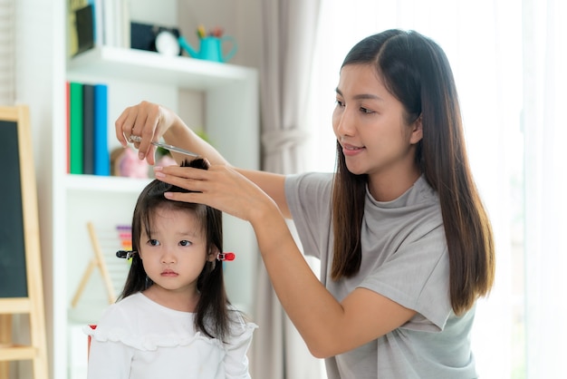 Mãe asiática cortando o cabelo da filha na sala de estar de casa